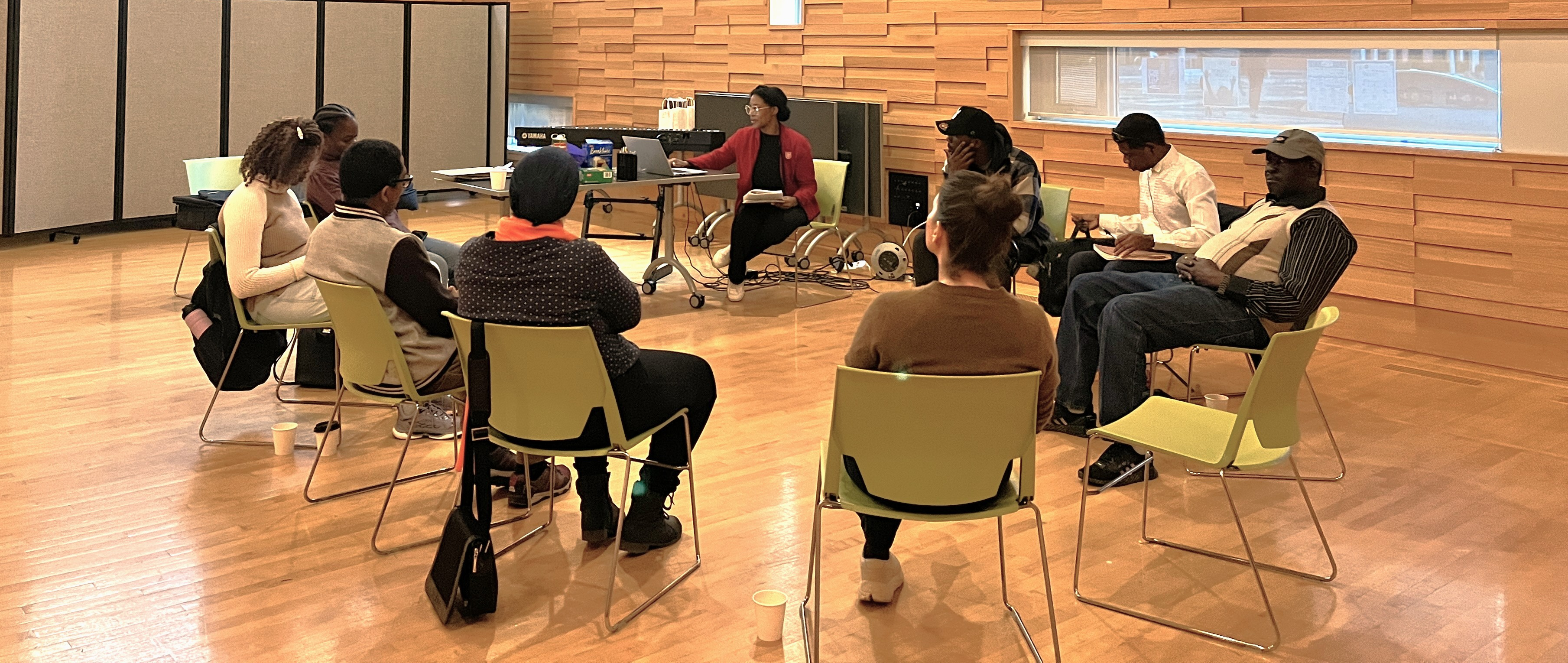Group of adults seated in a circle in a room, practicing conversational English together.