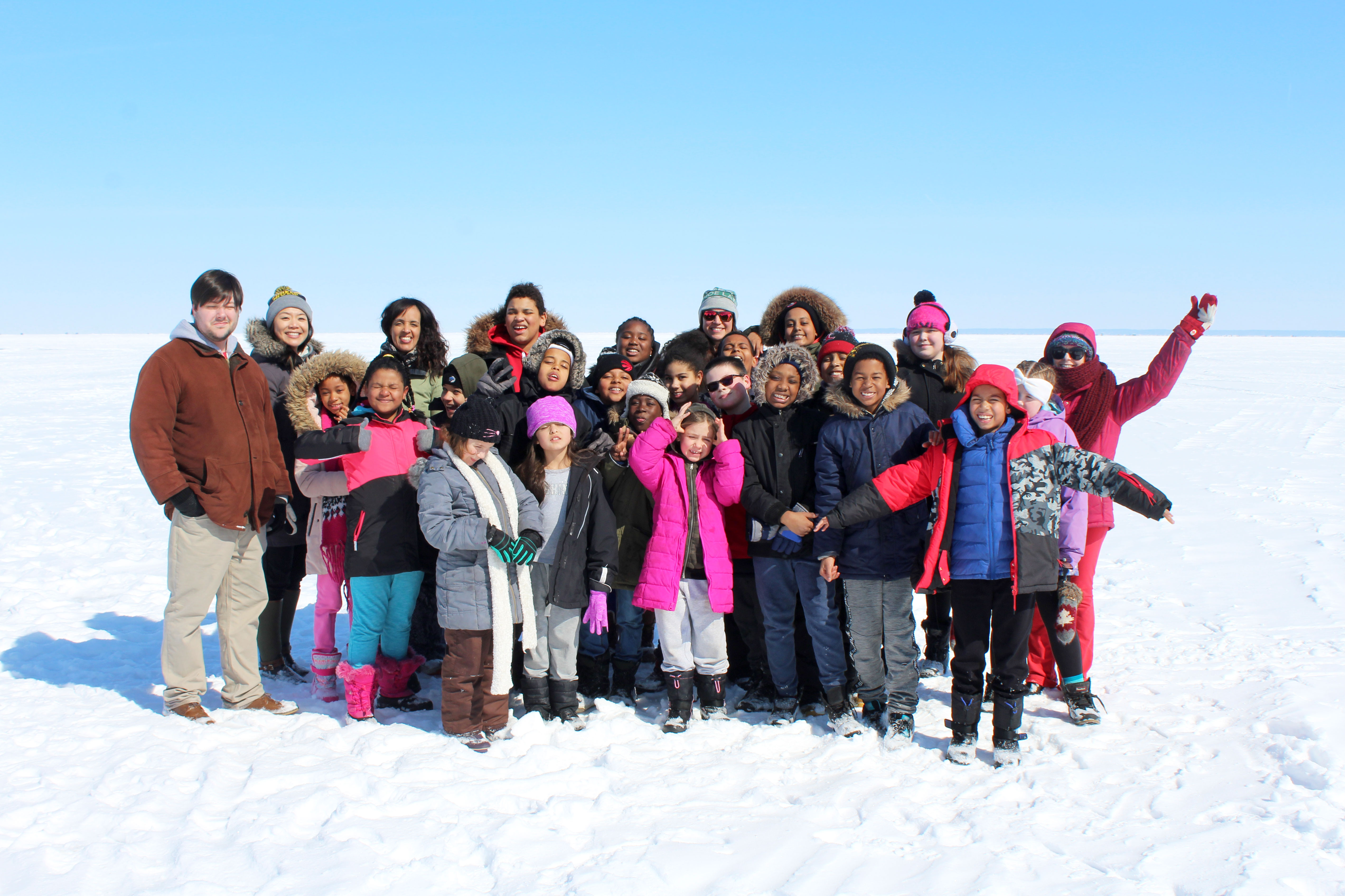 Group of children and program leaders standing together outdoors on a snowy field, smiling and posing for a group photo.