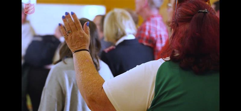 Person raising a hand in worship among a gathered community at Downtown East Community Church.