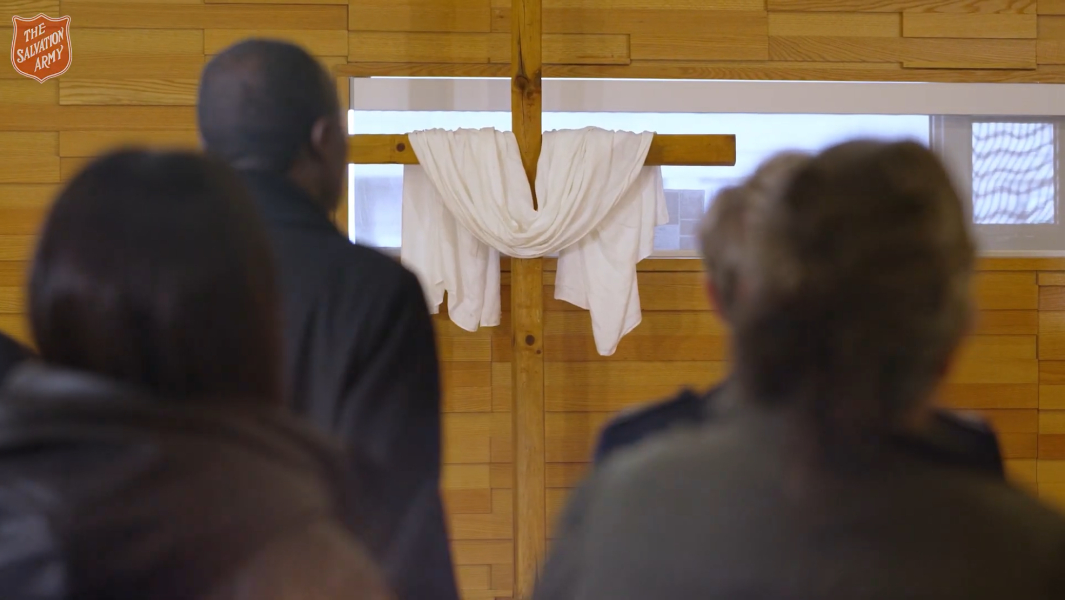 Congregants facing a wooden cross draped with white cloth inside the Downtown East Community Church worship space.