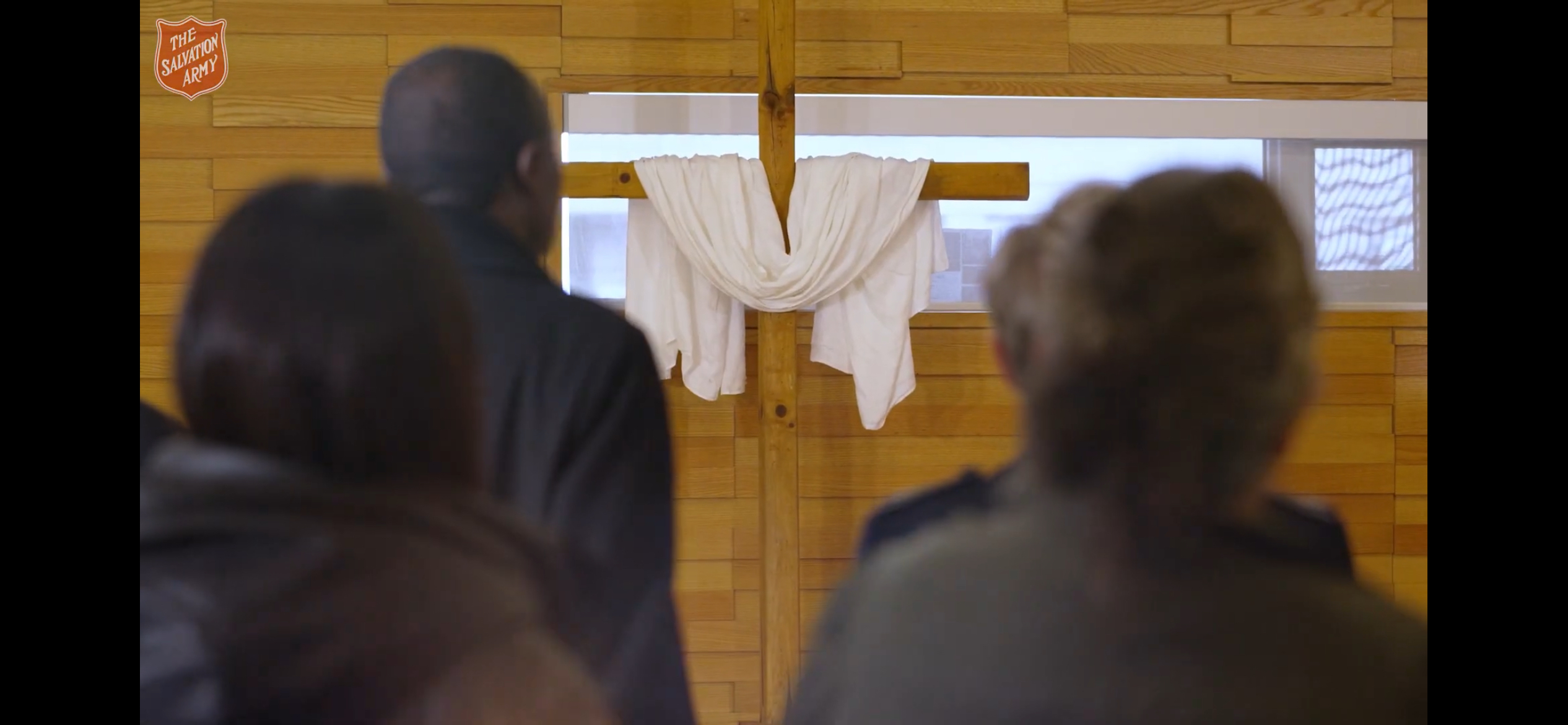 Congregants facing a wooden cross draped with white cloth inside the Downtown East Community Church worship space.