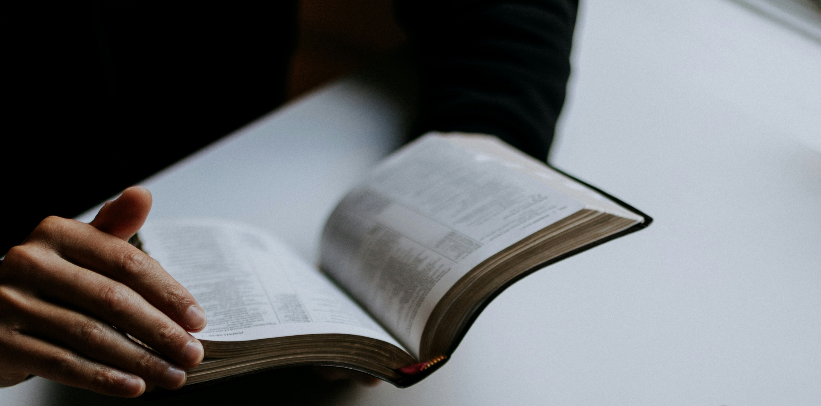 Open Bible held by an individual seated at a table.